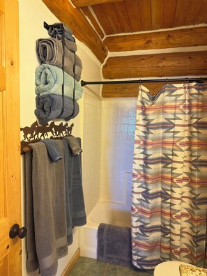 Een badkamer met een bad, een douchegordijn en handdoeken aan een rek.