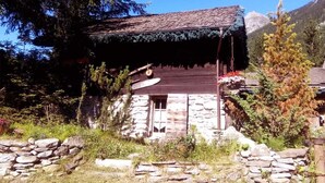 A rustic stone building with a sloped roof, surrounded by natural vegetation and a stone wall. - CANTATES CHALET with Private Jacuzzi on VRBO (Chamonix Mont-Blanc)