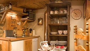 A rustic kitchen with wooden cabinets, a dining table set for two, and a clock on the wall. - CANTATES CHALET with Private Jacuzzi on VRBO (Chamonix Mont-Blanc)