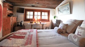 Una stanza accogliente con un letto, un armadietto in legno, un tavolo con una lampada e una finestra con tende.