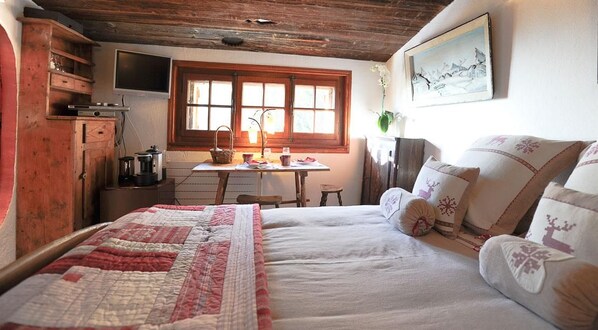 A cozy room with a bed, a wooden cabinet, a table with a lamp, and a window with curtains.