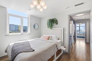 Ein modernes Schlafzimmer mit einem großen Bett, einer hängenden Pflanze und Blick auf die Stadt durch das Fenster.