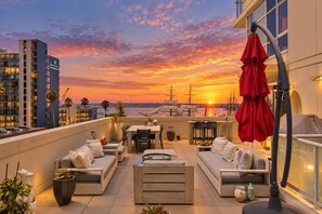 Eine Dachterrasse mit Außenmöbeln, Blick auf den Sonnenuntergang und einen Hafen im Hintergrund.