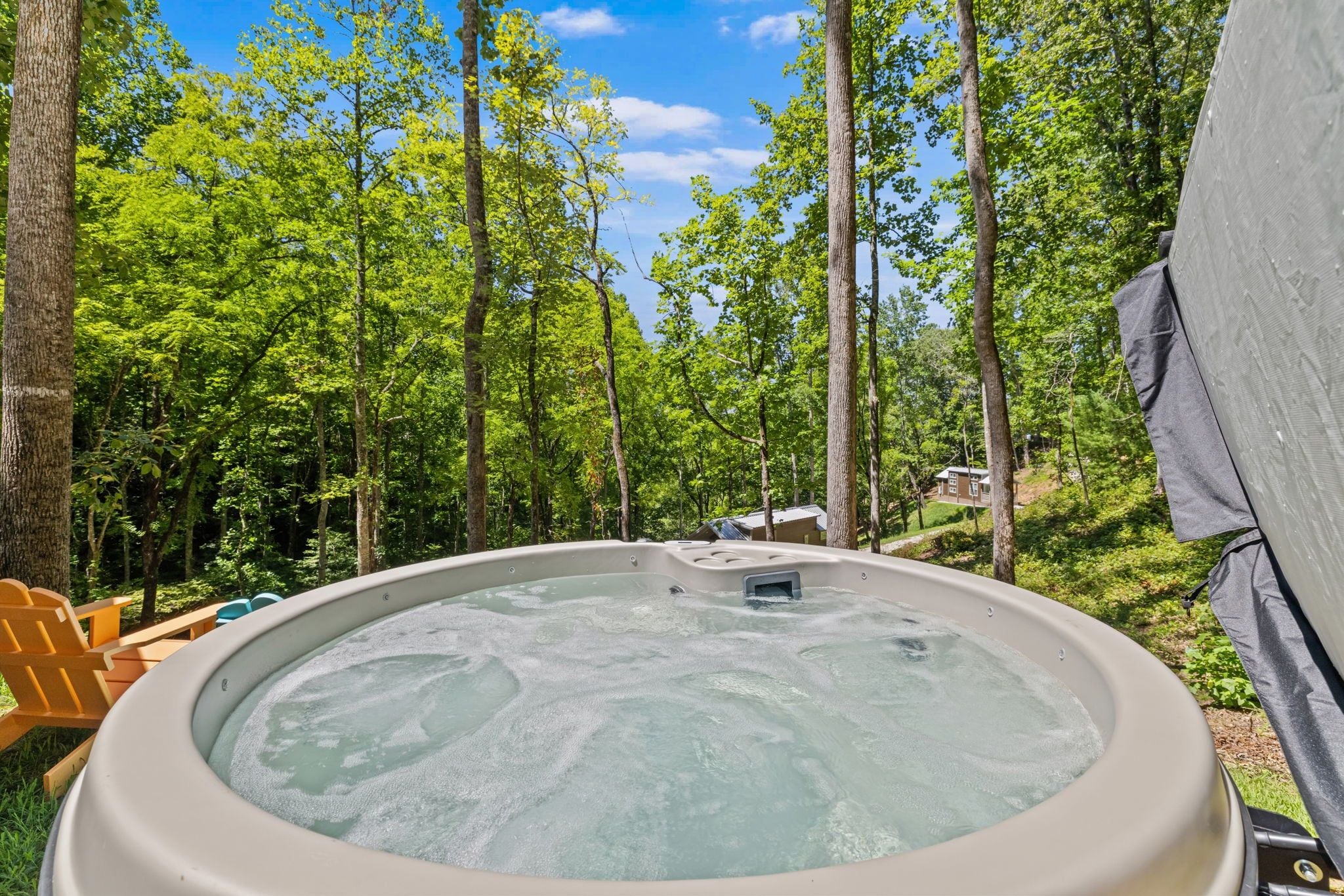 A hot tub surrounded by trees, with a tent and wooden chairs nearby.