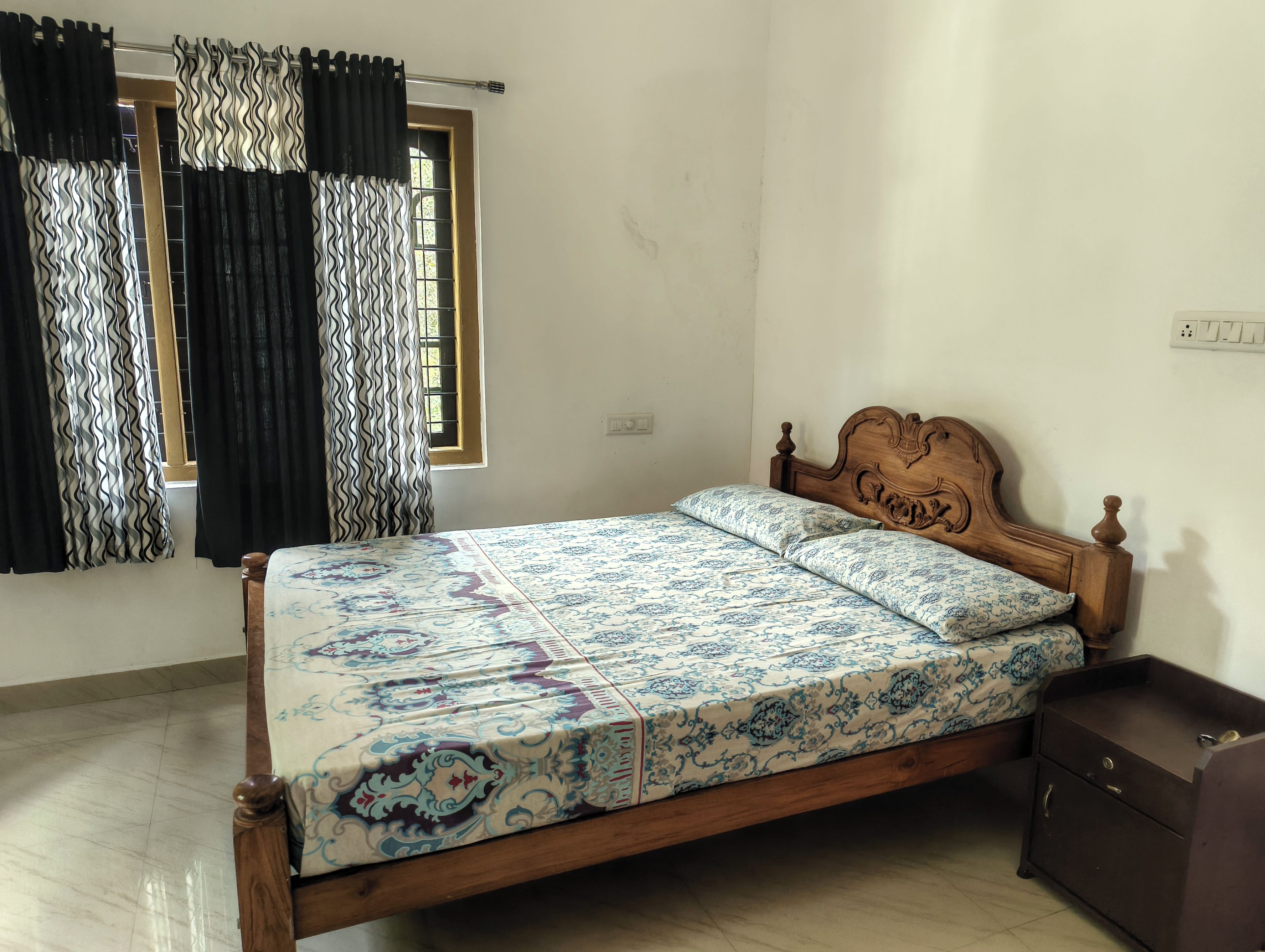 Una habitación con una cama de madera, un ventanal con barrotes y un enchufe en la pared.