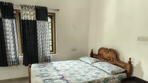 A room with a wooden bed, a window with metal bars, and a wall socket.