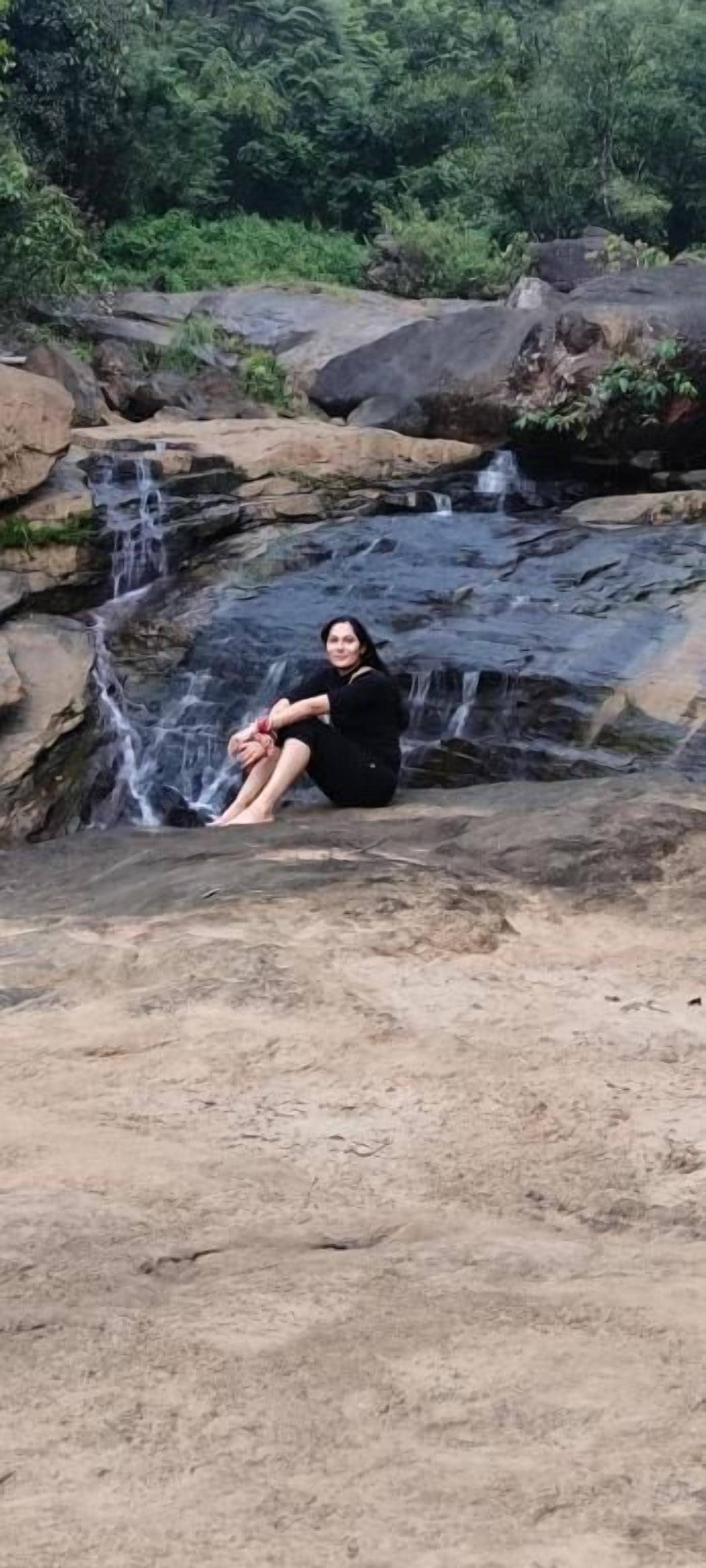 A person sitting on a rock by a waterfall in a natural setting.