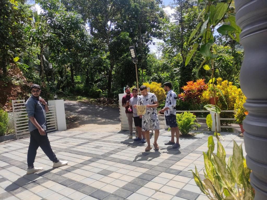 Un grupo de personas de pie en una zona pavimentada, con un jardín y árboles al fondo.