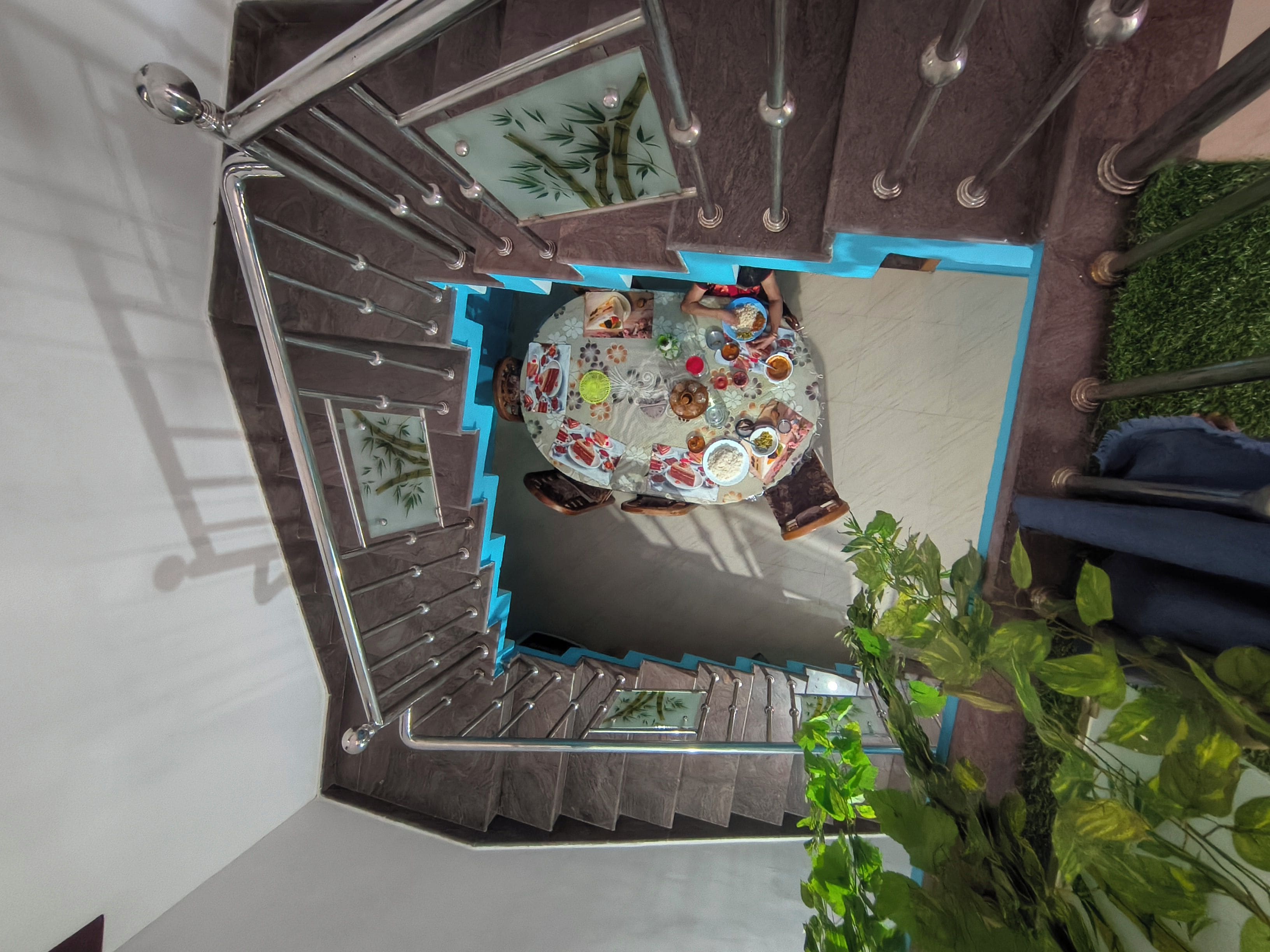 Una escalera de caracol con un comedor en la parte inferior, que incluye una mesa con diferentes platos y un panel de vidrio decorativo con motivos de bambú.