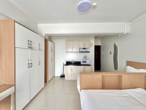 Ein modernes Schlafzimmer mit einem großen Bett, einem Holzschrank und einer kleinen Küche im Hintergrund.