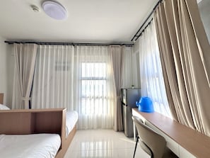 Ein Hotelzimmer mit einem Bett, einem Schreibtisch, einem Stuhl, einem Kühlschrank und Vorhängen.