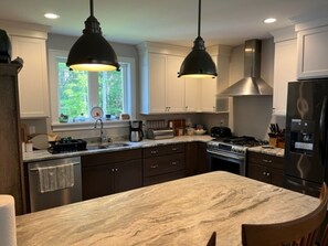 Une cuisine dotée d’un plan de travail en marbre, de meubles de couleur sombre, d’appareils électroménagers en acier inoxydable et de luminaires suspendus.
