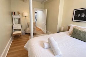 Een hotelkamer met een bed, een stoel, een bureau met spiegel, een lamp en een lijst aan de muur.