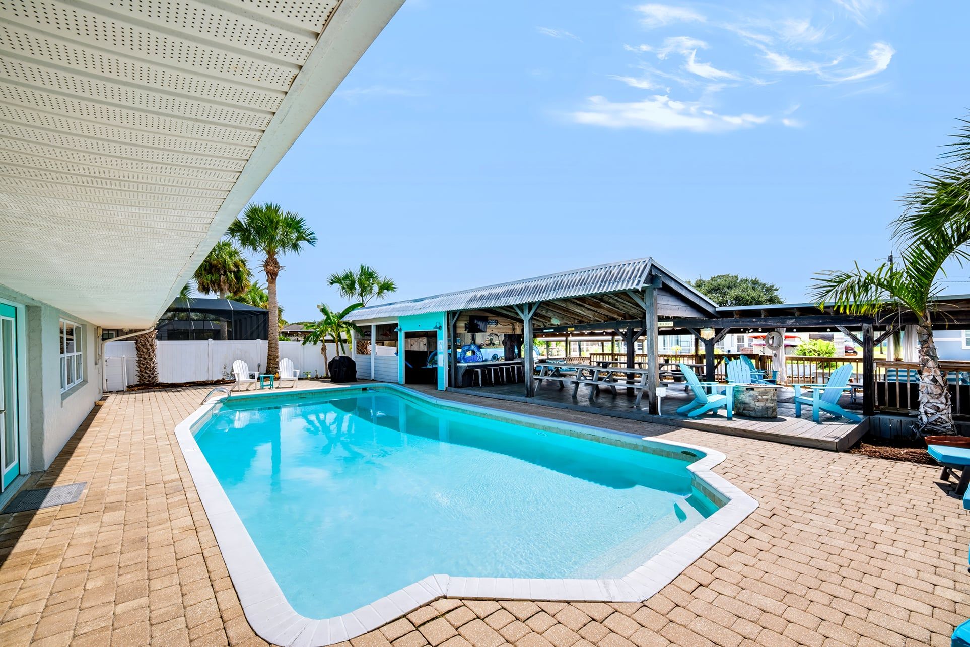 A swimming pool with a covered patio area, outdoor seating, and palm trees.