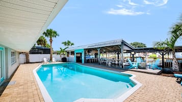 A swimming pool with a covered patio area, outdoor seating, and palm trees.