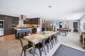 A spacious kitchen with modern appliances, a dining area with a pool table, and a living room with a large window.