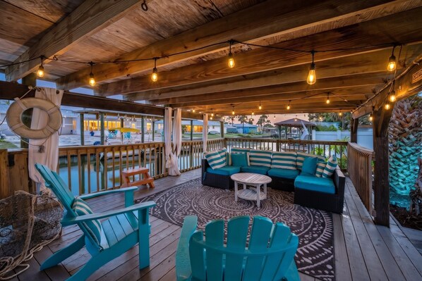 A covered outdoor seating area with a wooden deck, a sofa set, and a round table.
