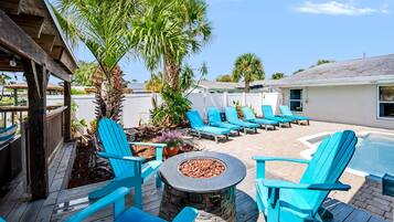An outdoor patio area with a fire pit, lounge chairs, and a pool.