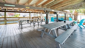 An outdoor covered picnic area with wooden benches and tables, a wooden deck, and a view of a water body. - Canal-Front Beach Home | 5BR/4BA | Private Pool + Boat Dock (Flagler Beach)