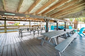 An outdoor covered picnic area with wooden benches and tables, a wooden deck, and a view of a water body. - Canal-Front Beach Home | 5BR/4BA | Private Pool + Boat Dock (Flagler Beach)