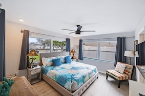 A bedroom with a bed, a chair, a ceiling fan, and a window. - Canal-Front Beach Home | 5BR/4BA | Private Pool + Boat Dock (Flagler Beach)
