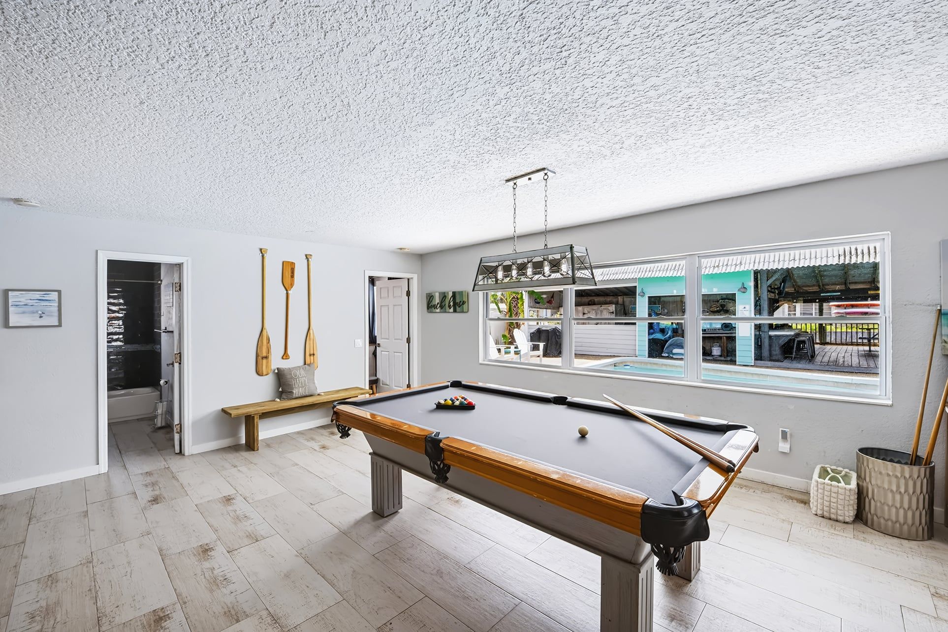 A pool table in a room with a view of a shop through a large window.