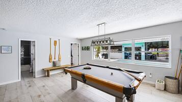 A pool table in a room with a view of a shop through a large window.