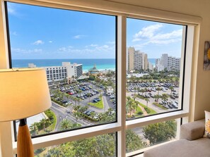 A room with a large window overlooking a parking lot and a beach. - Luau 2–6933 | 9th Floor Gulf Views | King + Sleeper Sofa | Tram Included (Miramar Beach)