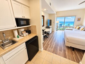 Eine moderne Küche mit Mikrowelle, Toaster und Spüle. Ein Essbereich mit Tisch und Stühlen ist zu sehen. Der Raum verfügt über ein großes Bett und Blick aufs Meer.