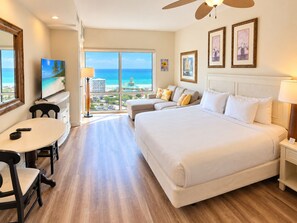 A hotel room with a large bed, a sofa, a dining table, and a TV. - Luau 2–6933 | 9th Floor Gulf Views | King + Sleeper Sofa | Tram Included (Miramar Beach)
