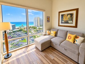 A living room with a large window, a sofa, and a lamp. - Luau 2–6933 | 9th Floor Gulf Views | King + Sleeper Sofa | Tram Included (Miramar Beach)