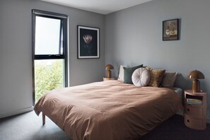 Ein Schlafzimmer mit einem großen Bett, zwei Nachttischen, einem Fenster und einem gerahmten Bild an der Wand.