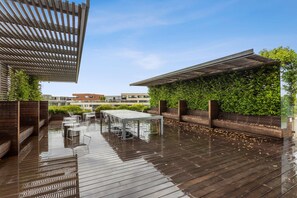 Eine Dachterrasse mit Holzdeck, Gartenmöbeln und einer Glasreling.