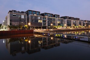 Ein modernes Gebäude mit mehreren Etagen und großen Fenstern, das sich in ruhigem Wasser spiegelt.