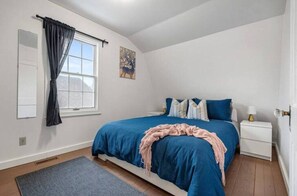 A bedroom with a bed, a nightstand, a window with curtains, a painting on the wall, and a rug on the floor. - Rosebud Farmhouse | Cozy Family & Friends Getaway (Rosebud)