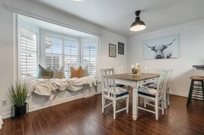 A dining area with a wooden table and white chairs, a window with blinds, and a ceiling light fixture. - Rosebud Farmhouse | Cozy Family & Friends Getaway (Rosebud)