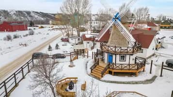 A traditional windmill with a wooden structure and a blue door, surrounded by a snowy landscape and a fenced area.
