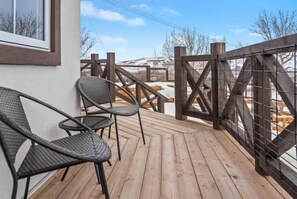Una terraza de madera con sillas y barandilla, con vistas a un paisaje nevado.