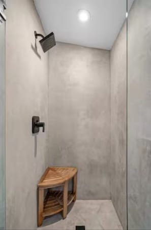 Una ducha moderna con cabezal de ducha de mano, un taburete de madera y un grifo empotrado en la pared.