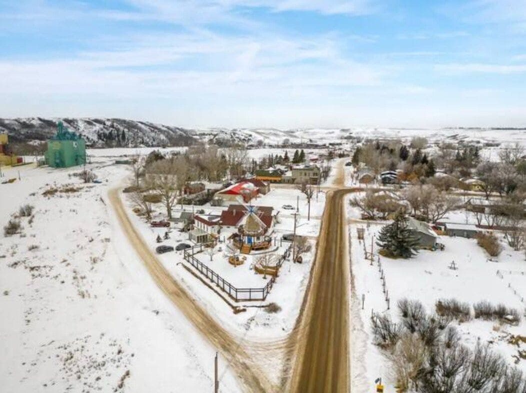 A rural landscape with a snow-covered road, buildings, and a green structure.