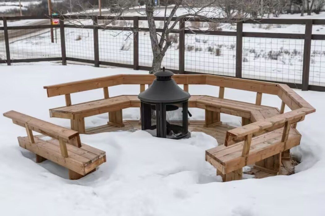 A wooden outdoor seating area with benches and a central fire feature.