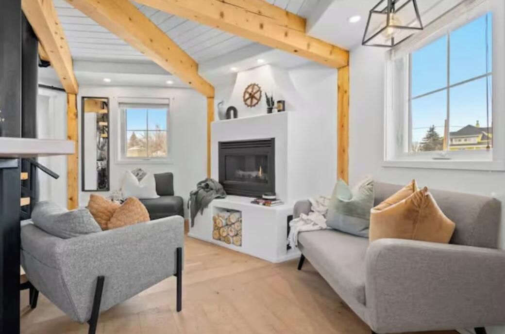 A modern living room with a fireplace, wooden beams, and large windows.