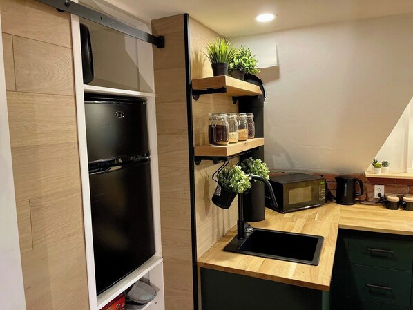 A modern kitchen with a built-in refrigerator, a microwave, and a sink. There are shelves with potted plants and jars.