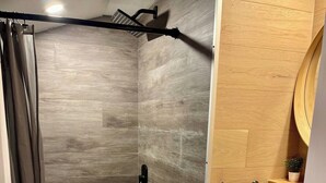 Un espace douche avec un mur en bois, une baignoire blanche et une petite étagère sur laquelle est posée une plante.