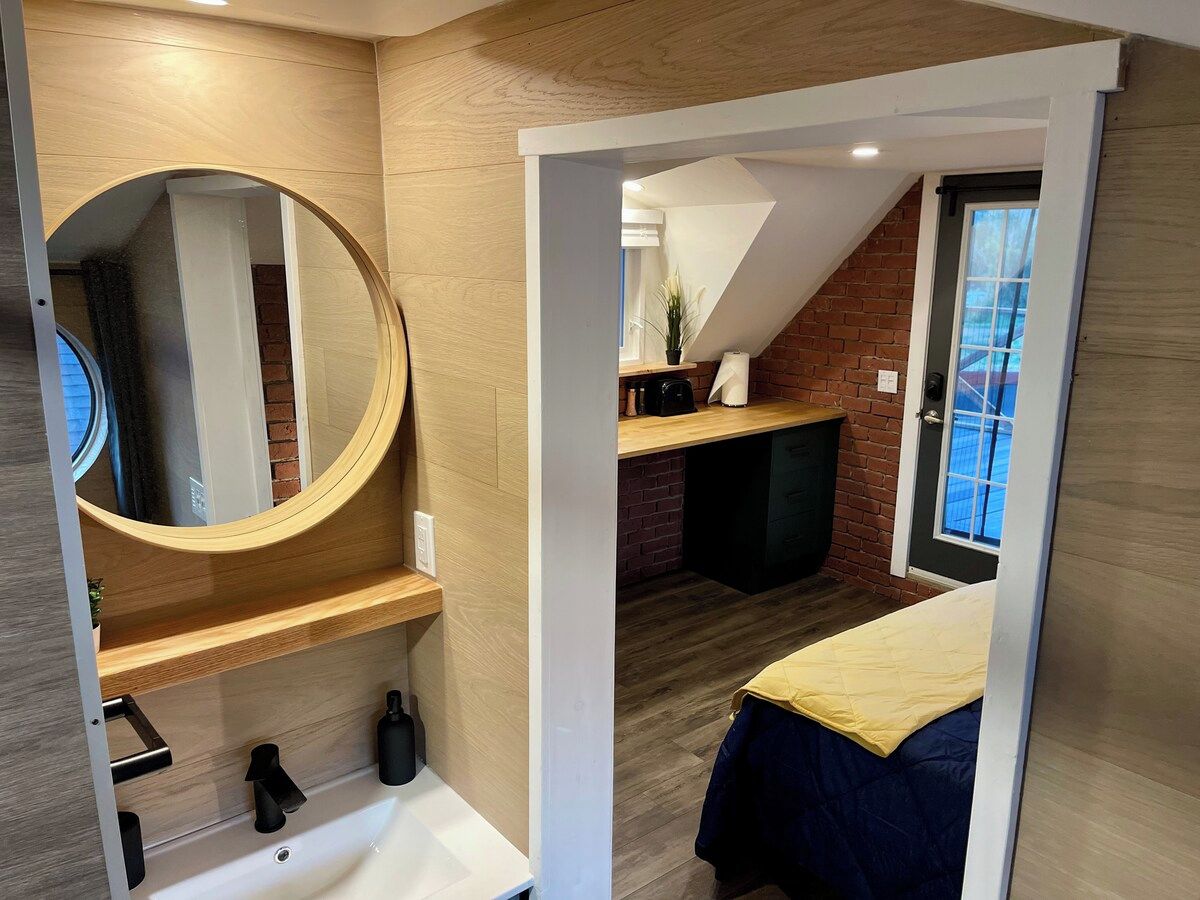 A bedroom with a bed, a round mirror, a wooden shelf, and a fireplace.