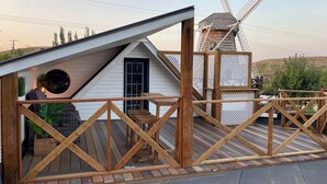 Une terrasse en bois avec un moulin à vent en arrière-plan, une petite maison avec un toit en pente et une clôture en bois.