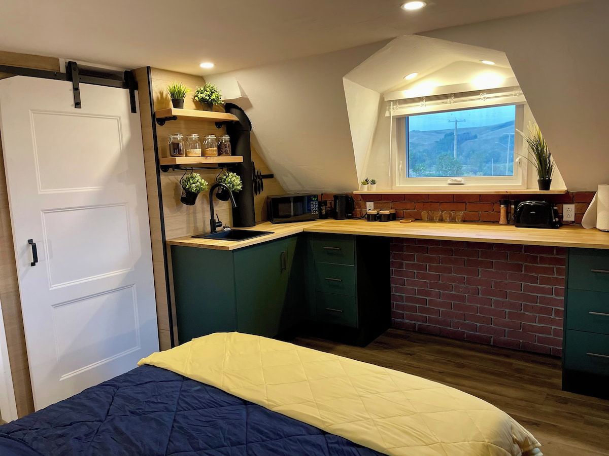 Ein kleines Zimmer mit Bett, Küchenzeile und Fenster mit Blick.