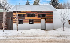 A two-story building with a sloped roof, a wooden fence, and a snow-covered ground. - Historic Firehall Guesthouse with Private Covered Patio & Wood Stove (Rosebud)