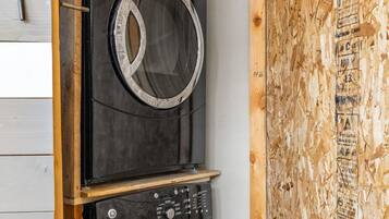 A compact laundry room with two stacked washing machines, wooden walls, and a visible door handle.