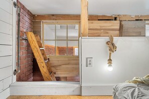 A room with a bed, a white wall, a wooden door, and a hanging rope.